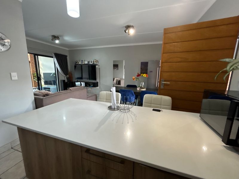 Open-plan living area featuring a modern kitchen island with stone countertops, flowing into a dining and lounge space with access to a patio.