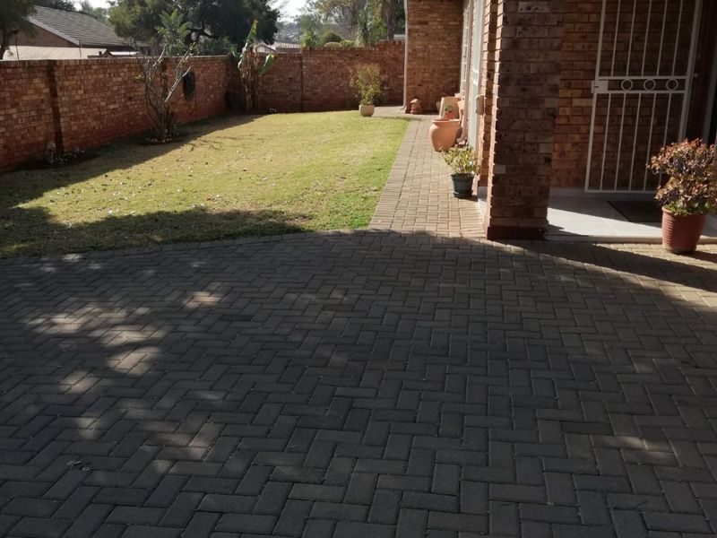 A rear exterior view of the townhouse featuring a paved patio area, a small lawn, and a secure brick boundary wall.