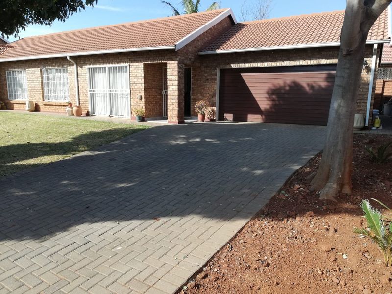 Front view of a brick townhouse featuring a tiled roof, paved driveway, and an integrated double garage with a brown sectional door.