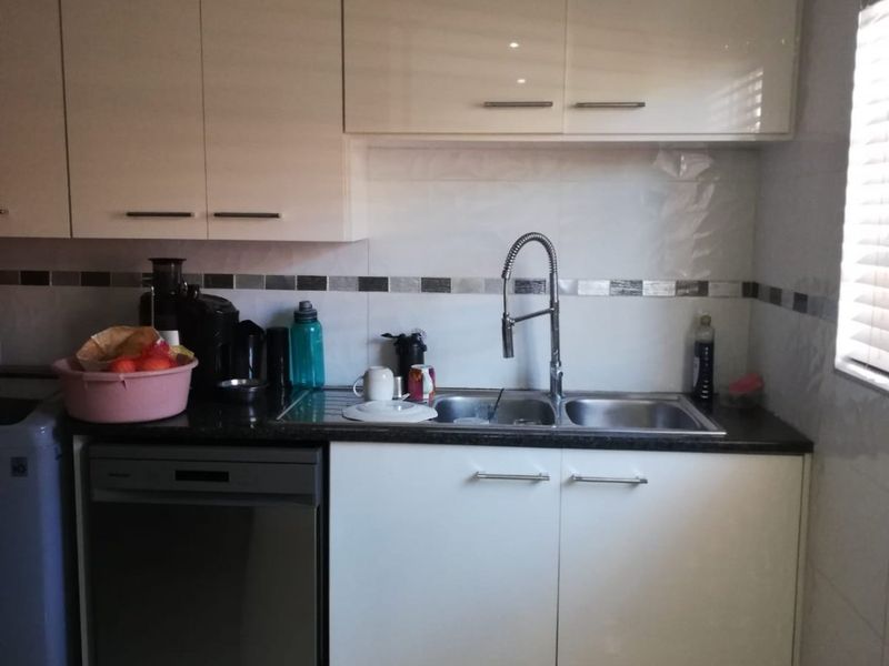 A functional kitchen area featuring modern white cabinetry, a stainless steel sink with a gooseneck faucet, and a built-in dishwasher.