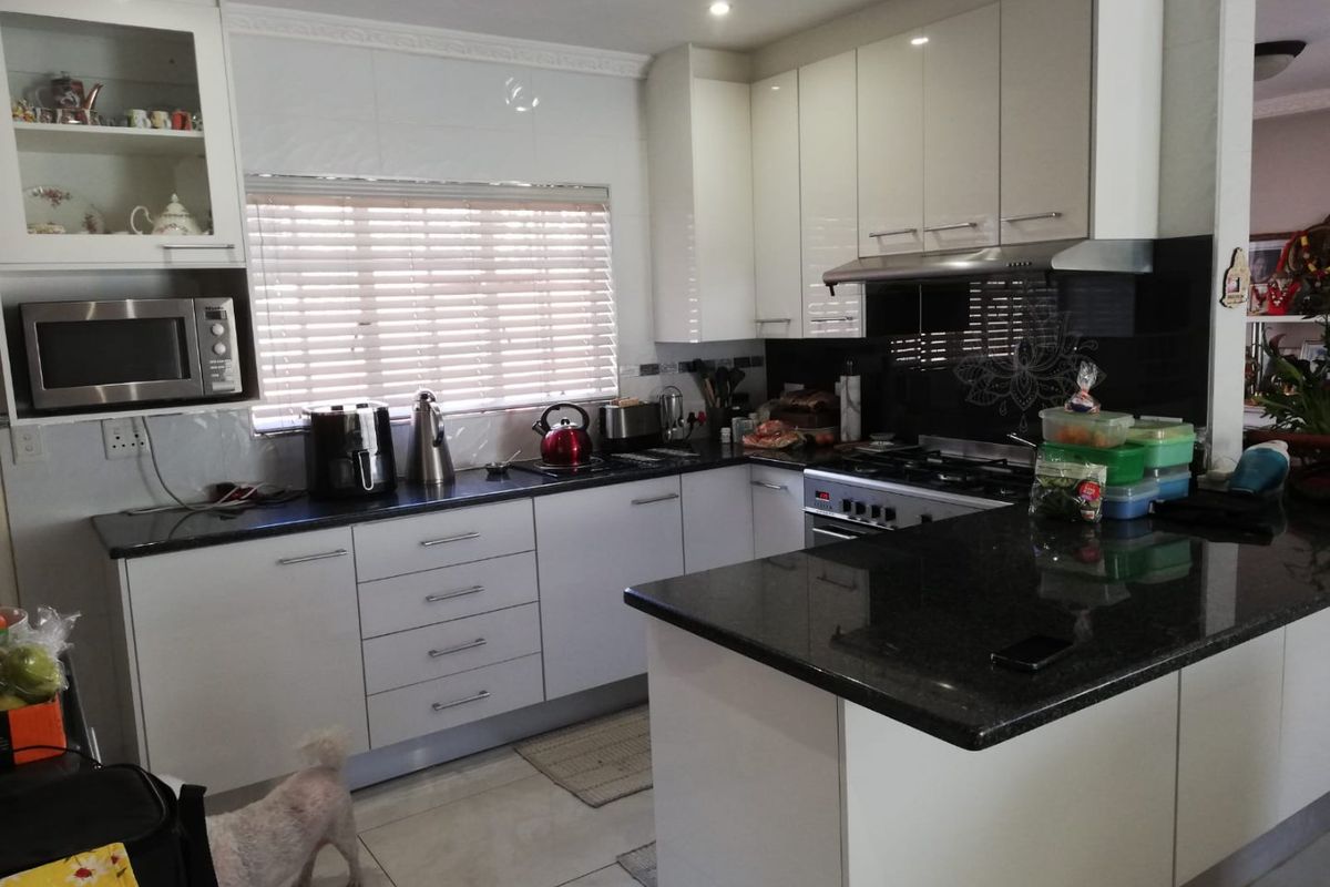 Modern kitchen featuring high-gloss cabinetry, granite countertops, a gas hob with extractor fan, and built-in microwave, offering a clean and functional workspace.