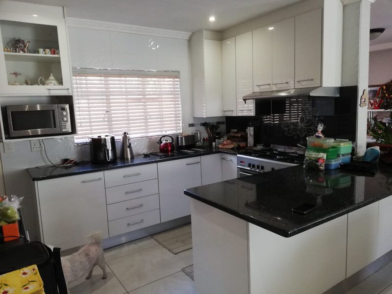 Modern kitchen featuring high-gloss cabinetry, granite countertops, a gas hob with extractor fan, and built-in microwave, offering a clean and functional workspace.