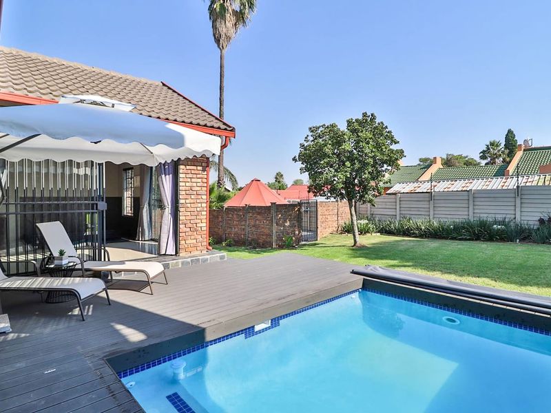 Outdoor entertainment area featuring a swimming pool, timber decking, and a well-maintained garden with brick boundary walls.