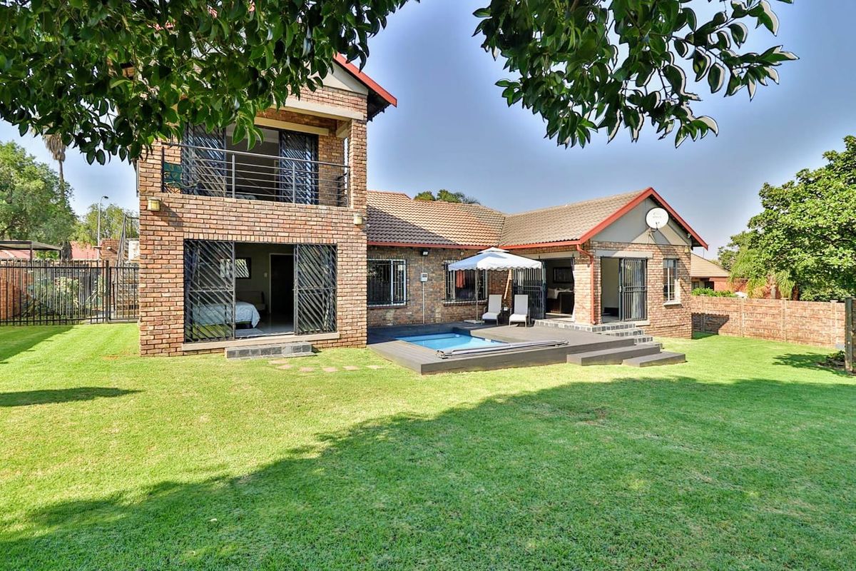 Rear view of a double-story face brick house featuring a swimming pool, timber deck, and an upper-level balcony overlooking a spacious garden.