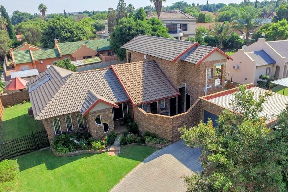 Aerial view of a well-maintained face brick house featuring a tiled roof, paved driveway, attached garage, and established garden in a residential estate.