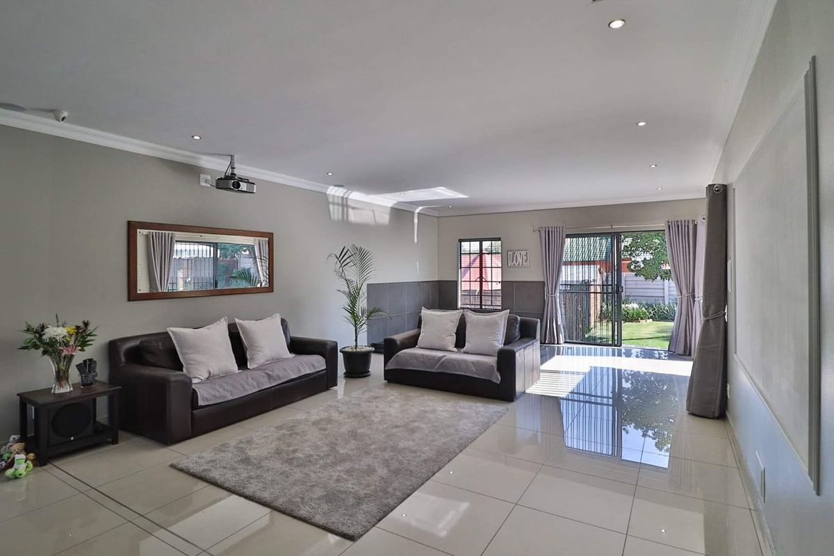 Spacious living room featuring polished tiled flooring, recessed downlighting, and direct access to the rear garden through a sliding glass door.