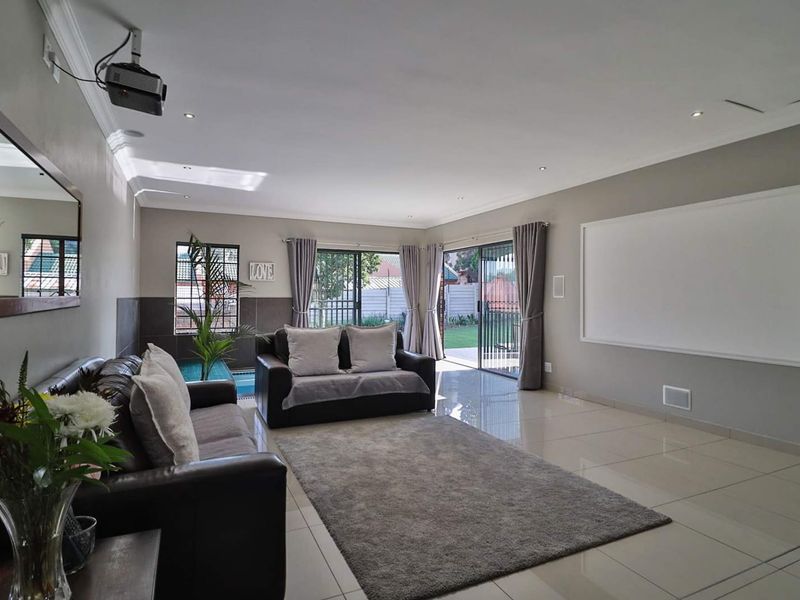 Spacious living room featuring large format floor tiles, recessed lighting, and integrated projector setup with direct access to the outdoor pool area.