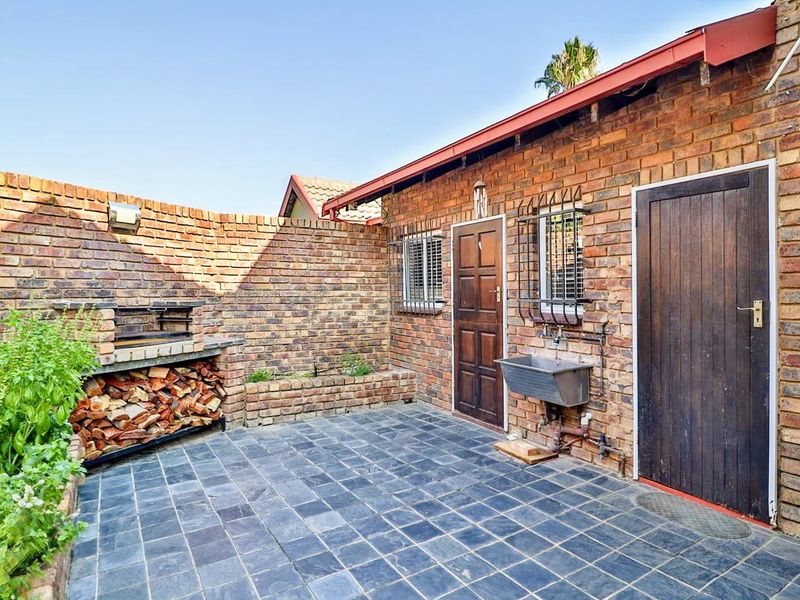 A private outdoor patio area featuring a built-in brick braai, slate tile flooring, and a functional utility sink against a rustic brick facade.