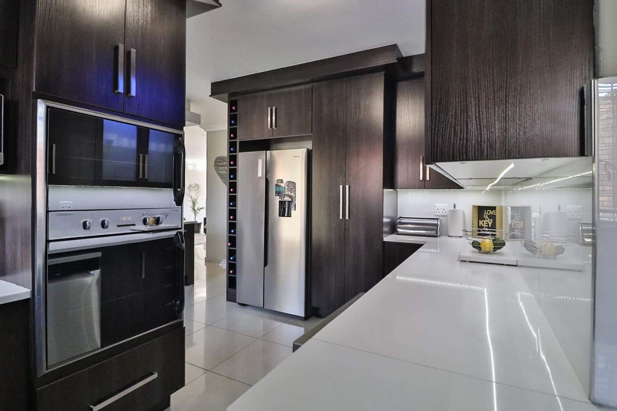 Modern kitchen featuring dark wood cabinetry, sleek white stone countertops, integrated appliances, and under-cabinet lighting, creating a sophisticated and functional culinary space.