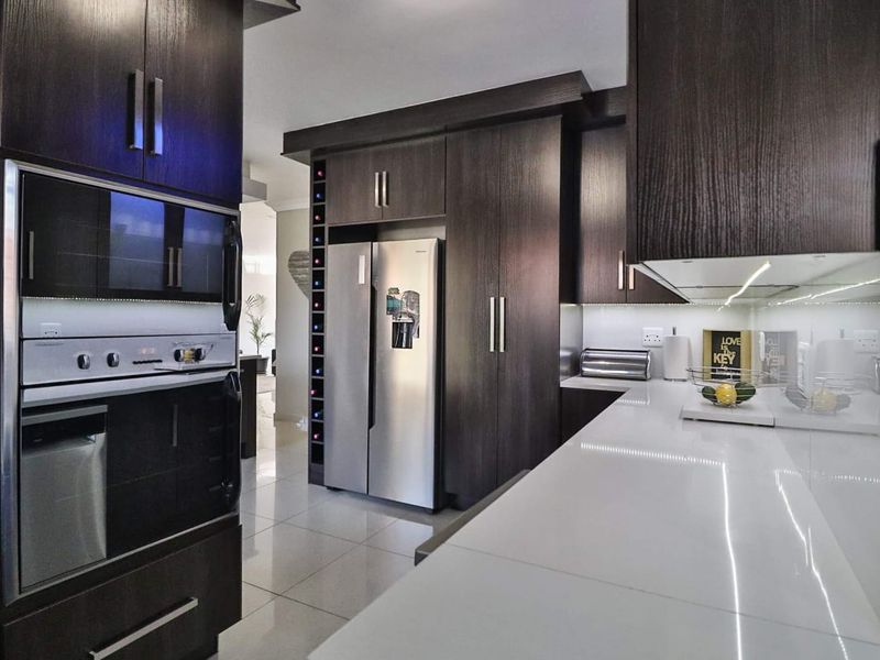 Modern kitchen featuring dark wood cabinetry, sleek white stone countertops, integrated appliances, and under-cabinet lighting, creating a sophisticated and functional culinary space.