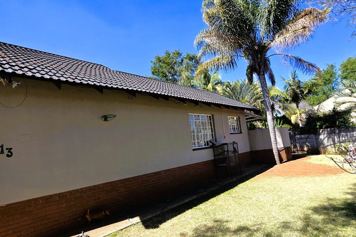 A view of the rear exterior of the house featuring a tiled roof, brick base, and security bars on the windows.