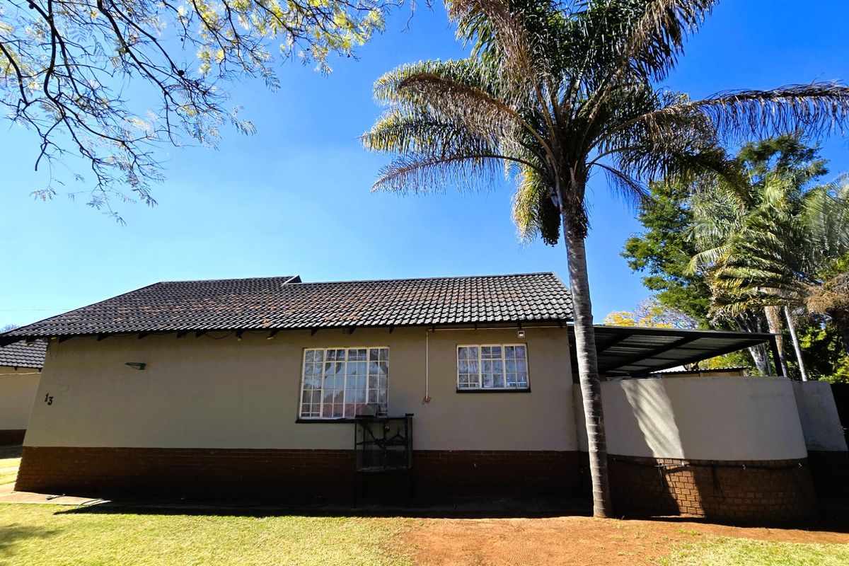 Rear view of a single-story house featuring a tiled roof, steel-framed windows, and a covered patio area set within a garden.