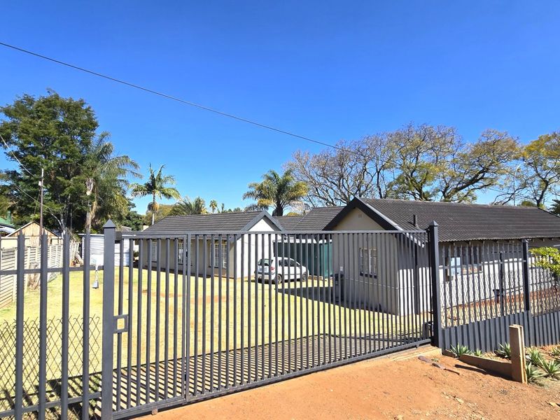 Front view of the property featuring a secure metal gate, perimeter fencing, and a well-maintained driveway leading to the main house structure.