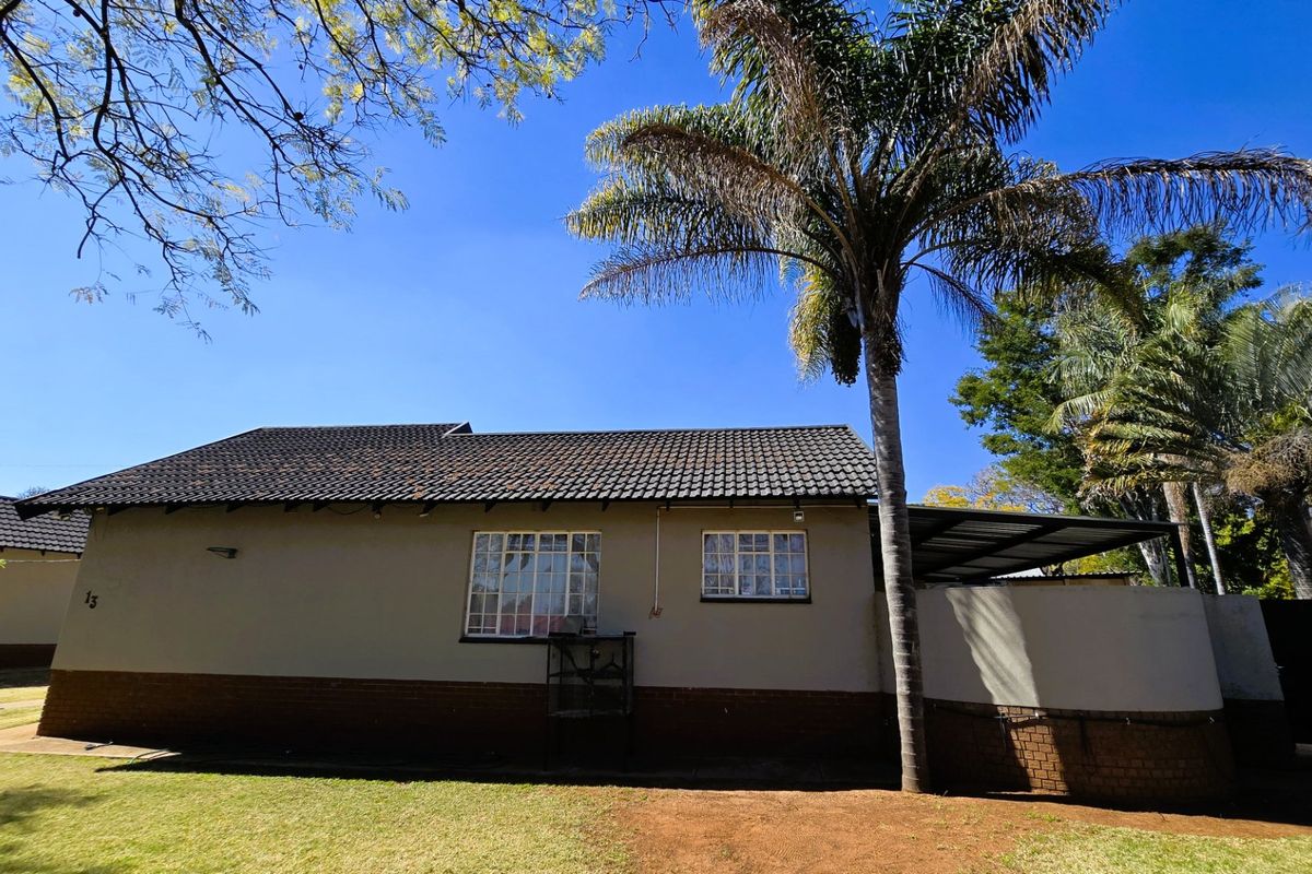 Rear view of the house featuring a tiled roof, brick base, and a covered patio area set within a garden.