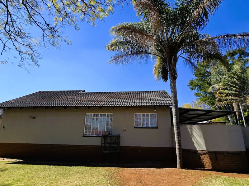 Rear view of the house featuring a tiled roof, brick base, and a covered patio area set within a garden.