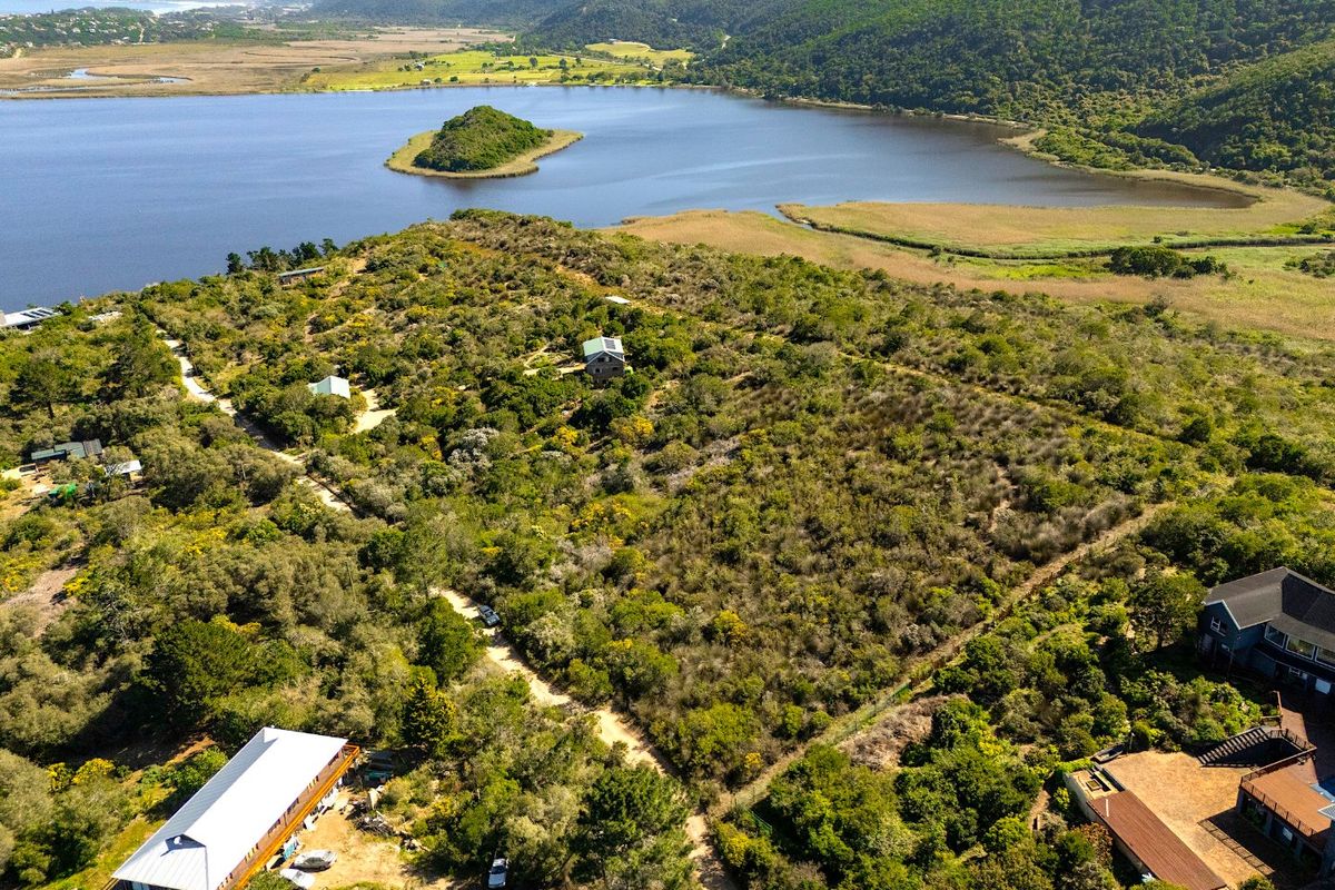 An aerial view of a large, undeveloped residential plot featuring natural vegetation, dirt access paths, and scenic proximity to the lagoon and surrounding hills.