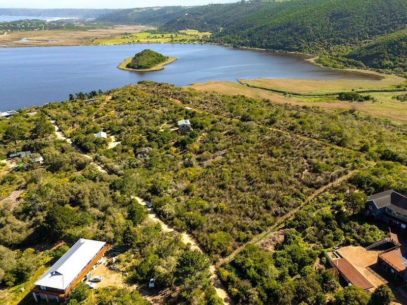 An aerial view of a large, undeveloped residential plot featuring natural vegetation, dirt access paths, and scenic proximity to the lagoon and surrounding hills.