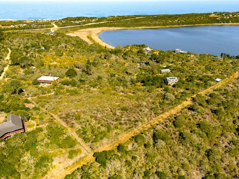 An aerial view of a coastal residential plot featuring natural vegetation, lake frontage, and proximity to the ocean.