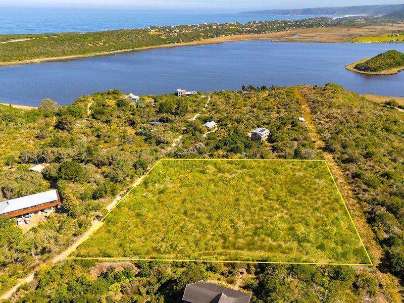 An aerial view of a vacant residential plot featuring natural vegetation, situated in a scenic coastal area with water views.