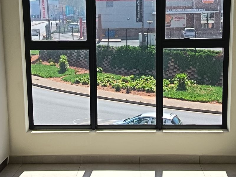 A bright, empty interior space featuring large aluminium-framed windows with a direct view of the street and surrounding commercial area.