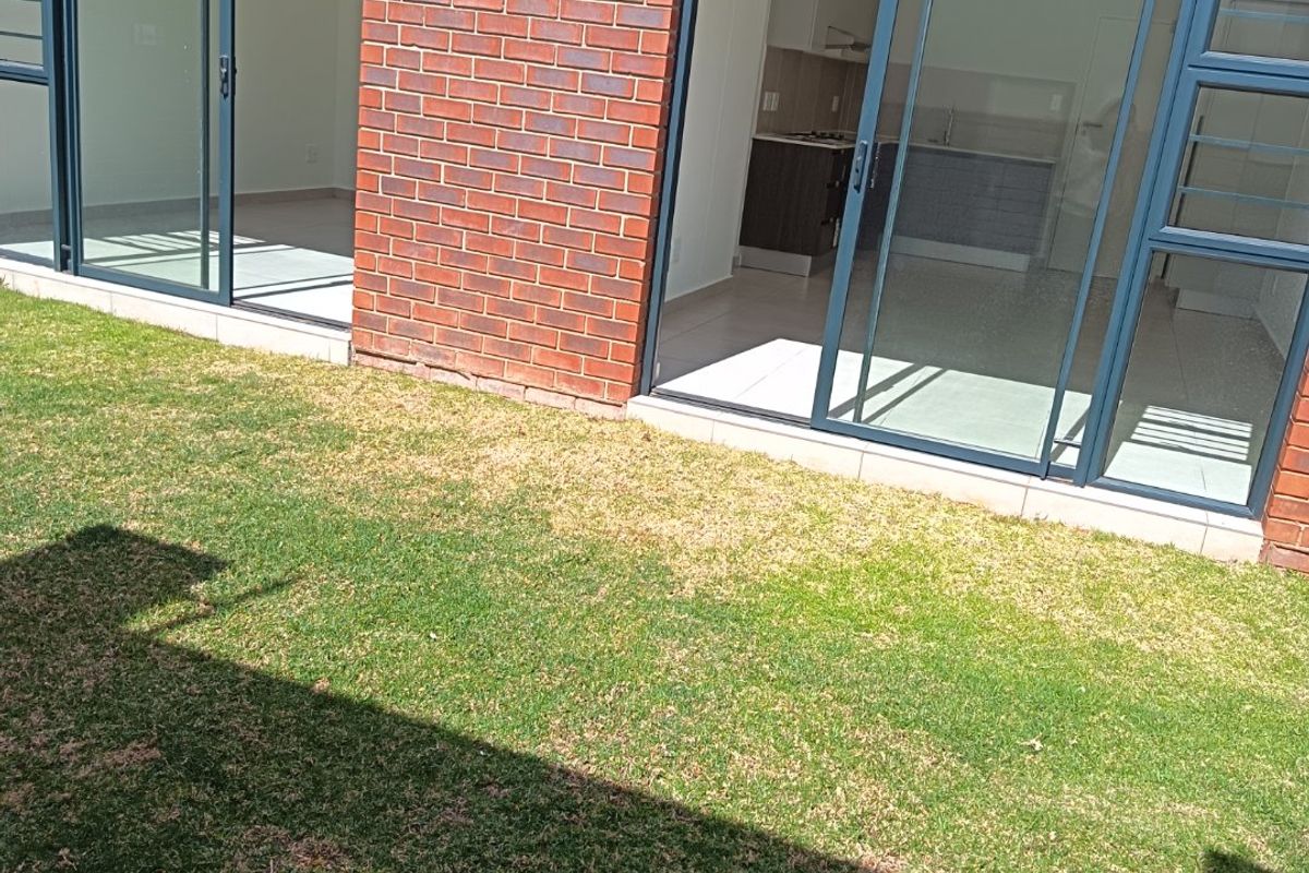 Rear view of an apartment featuring an exposed brick facade, sliding glass doors providing access to the interior, and a private lawn area.