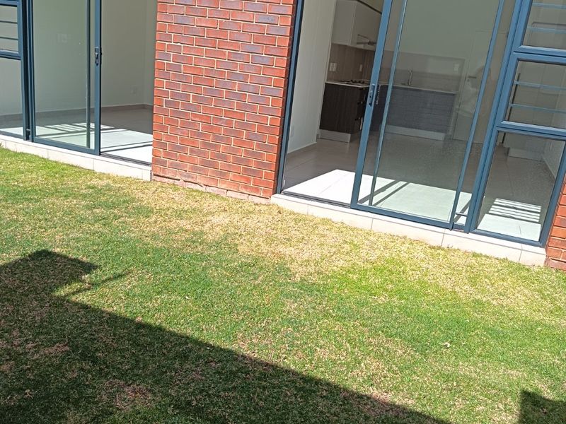 Rear view of an apartment featuring an exposed brick facade, sliding glass doors providing access to the interior, and a private lawn area.