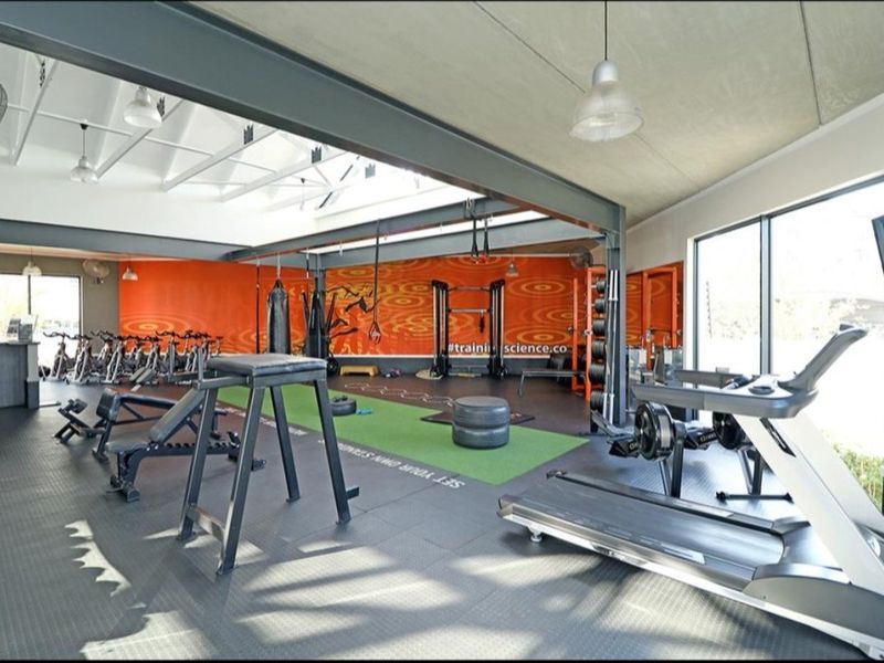 Spacious, well-equipped gym featuring industrial-style exposed steel beams, durable rubber flooring, and large windows providing ample natural light.