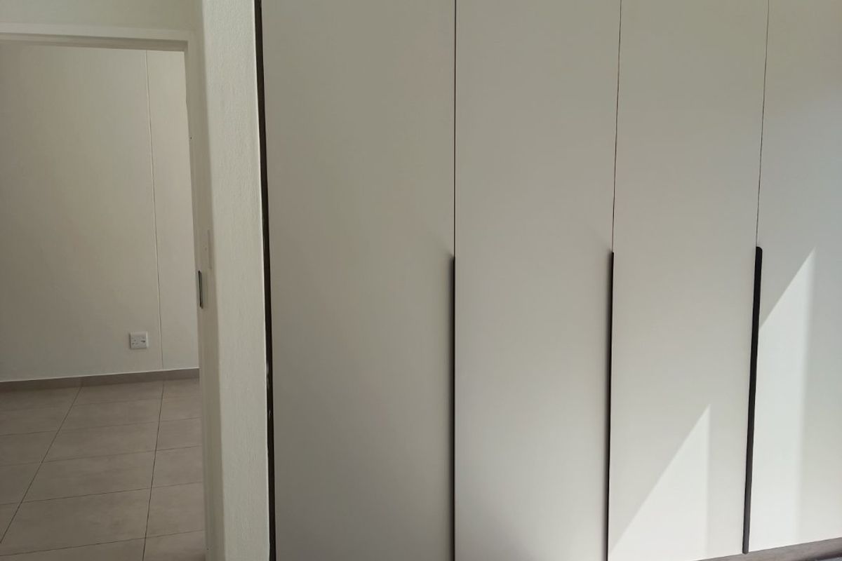 A bright bedroom featuring modern built-in cupboards with a contrasting dark trim and neutral tiled flooring throughout.