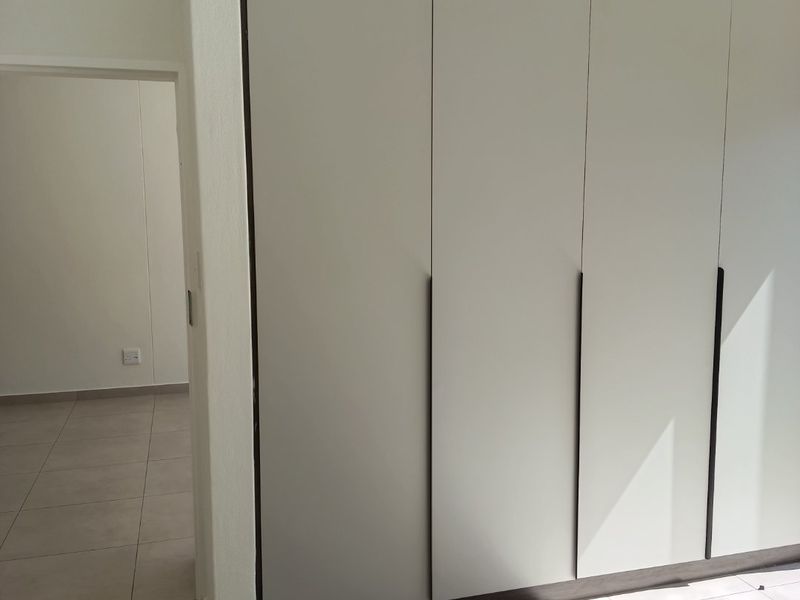 A bright bedroom featuring modern built-in cupboards with a contrasting dark trim and neutral tiled flooring throughout.