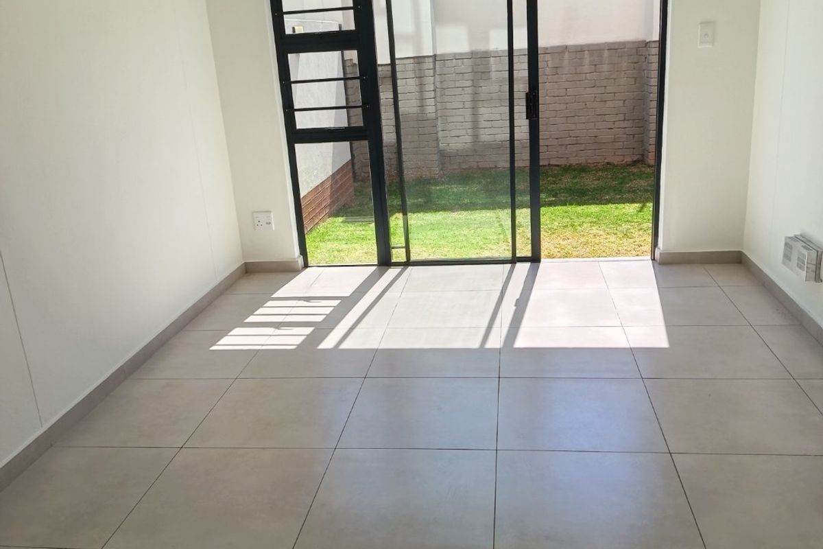 A bright, empty living room featuring neutral tiled flooring and a large sliding glass door providing direct access to the rear garden.