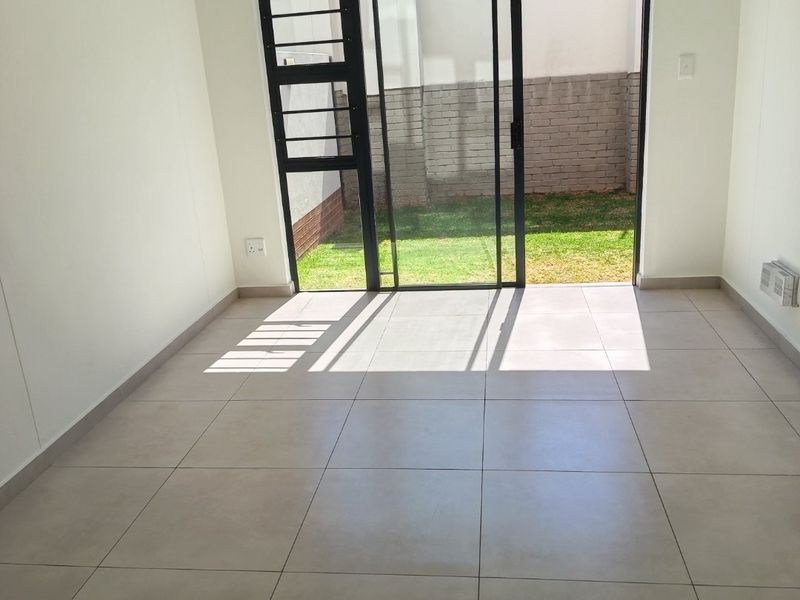 A bright, empty living room featuring neutral tiled flooring and a large sliding glass door providing direct access to the rear garden.