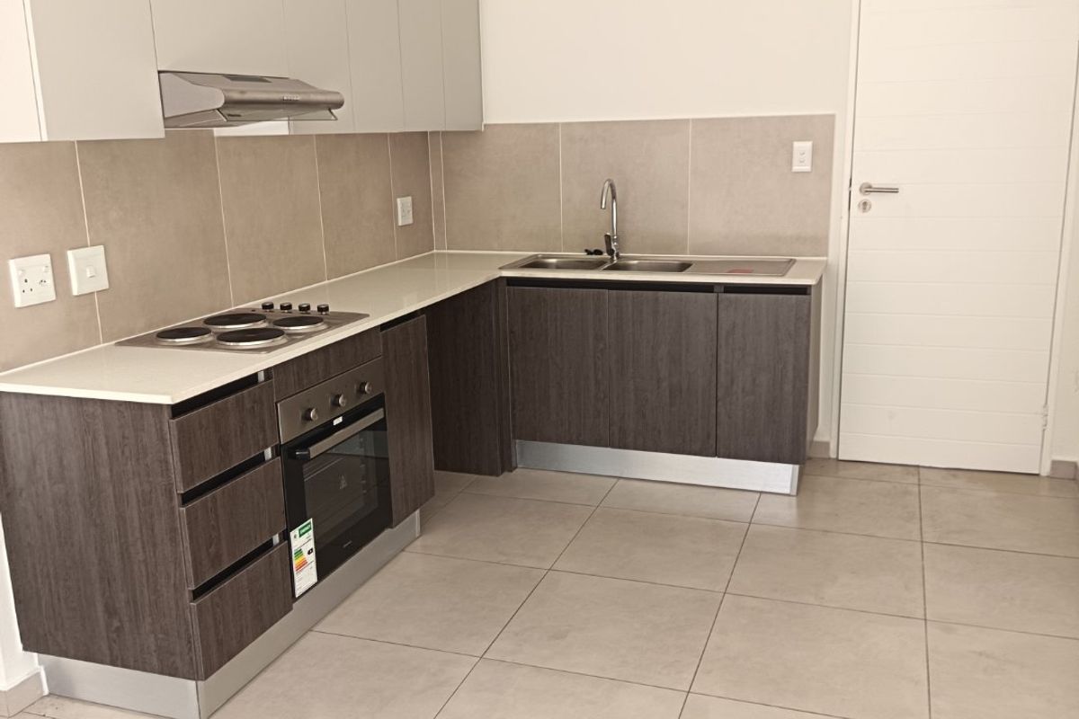 Modern kitchen featuring dark wood lower cabinets, light upper cabinets, stone countertops, integrated oven, electric hob, and neutral tiled flooring.