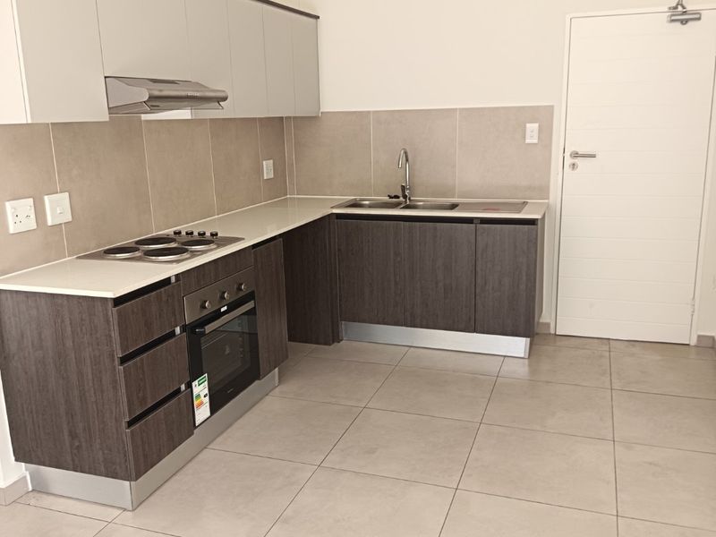 Modern kitchen featuring dark wood lower cabinets, light upper cabinets, stone countertops, integrated oven, electric hob, and neutral tiled flooring.