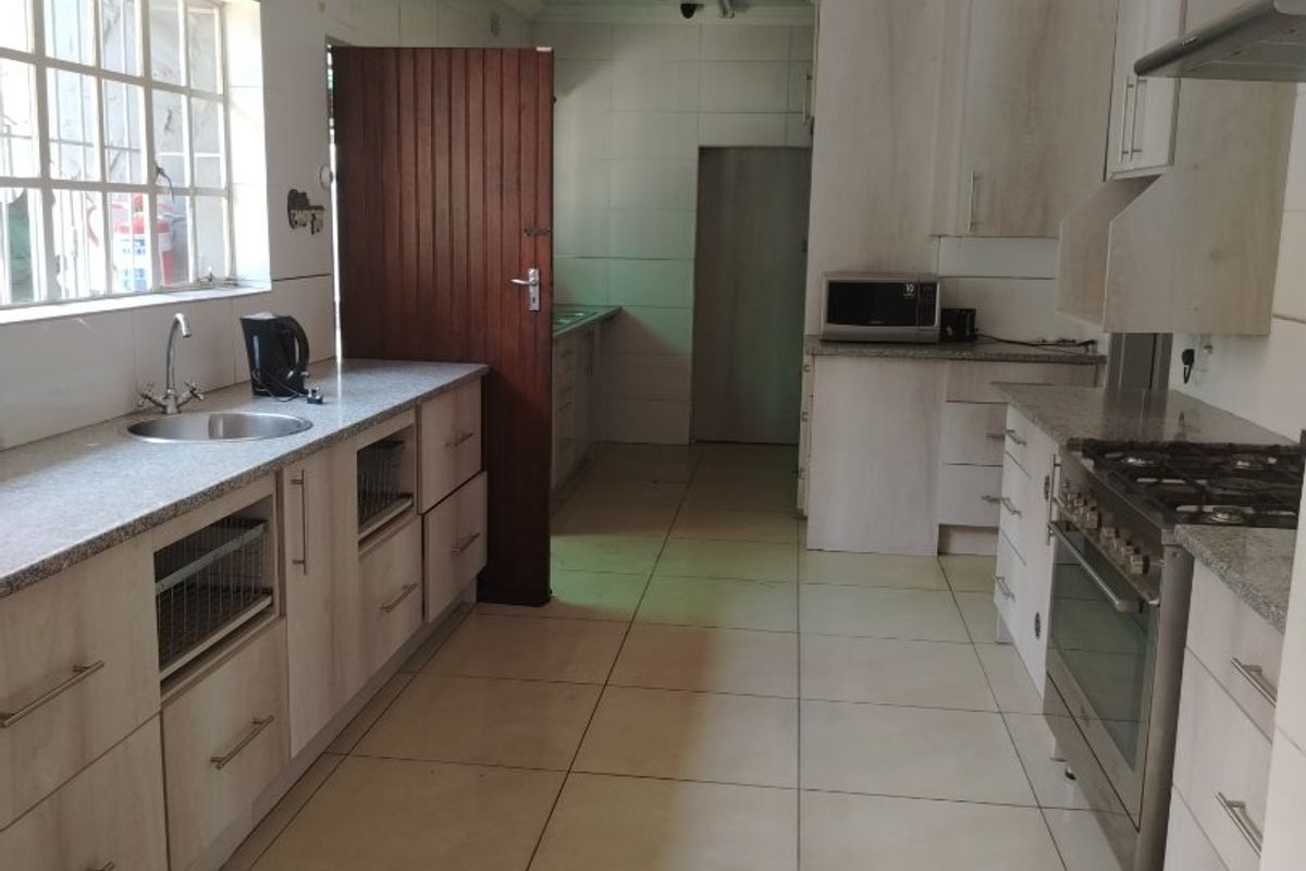 A functional kitchen featuring light-toned cabinetry, granite countertops, a stainless steel gas stove, and tiled flooring with a separate scullery area.