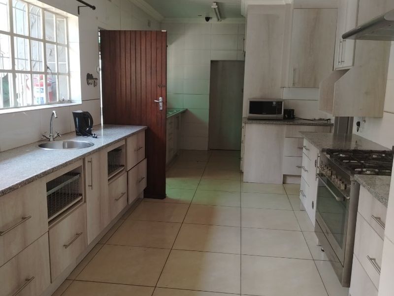 A functional kitchen featuring light-toned cabinetry, granite countertops, a stainless steel gas stove, and tiled flooring with a separate scullery area.