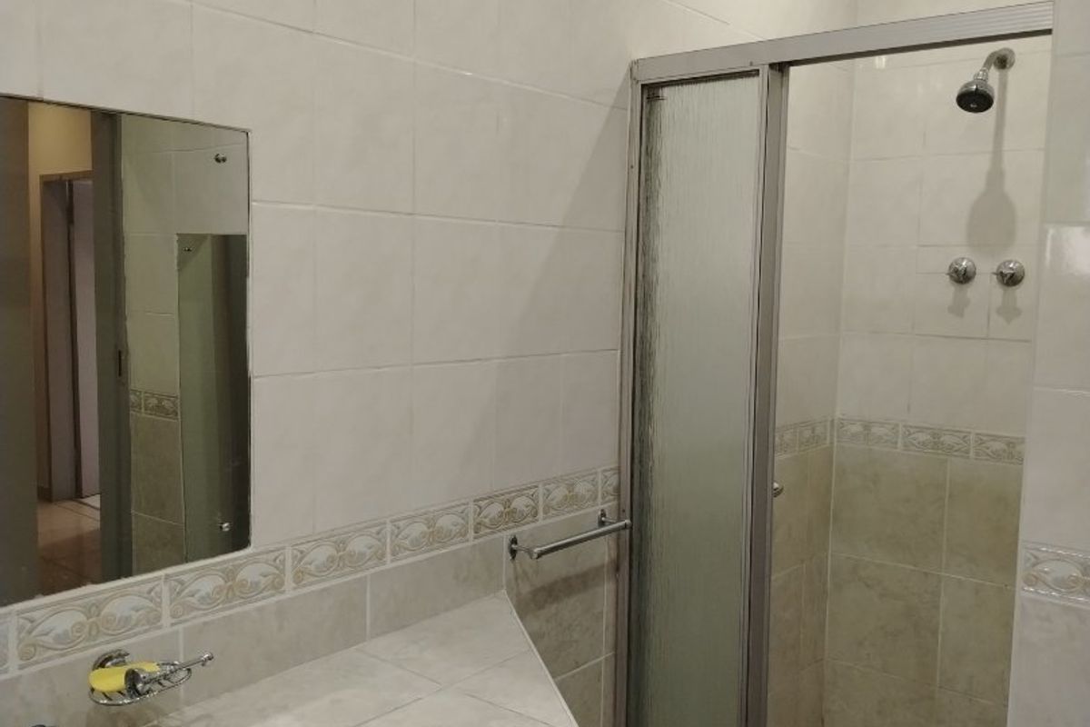 A functional bathroom featuring a tiled vanity with an integrated sink, a glass-enclosed shower, and neutral wall tiling throughout.