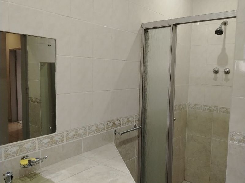 A functional bathroom featuring a tiled vanity with an integrated sink, a glass-enclosed shower, and neutral wall tiling throughout.