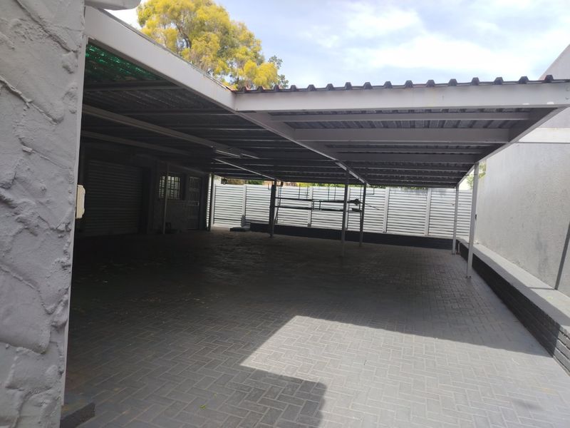 A spacious, paved covered carport area featuring a metal roof structure and secure perimeter fencing, providing ample off-street parking space.