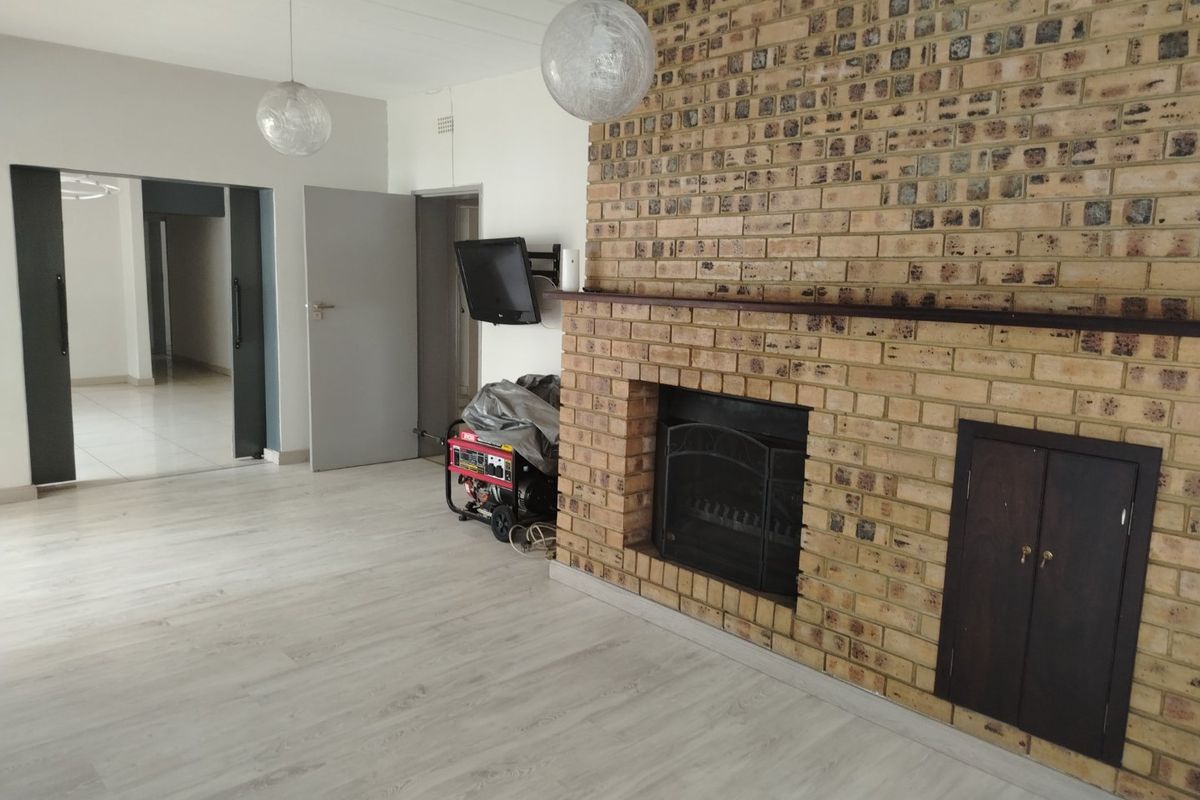 Spacious living room featuring a prominent face-brick fireplace with a mantel, light-toned laminate flooring, and neutral wall finishes.