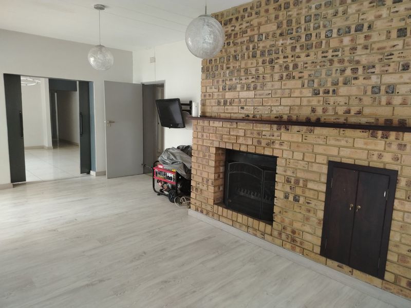 Spacious living room featuring a prominent face-brick fireplace with a mantel, light-toned laminate flooring, and neutral wall finishes.