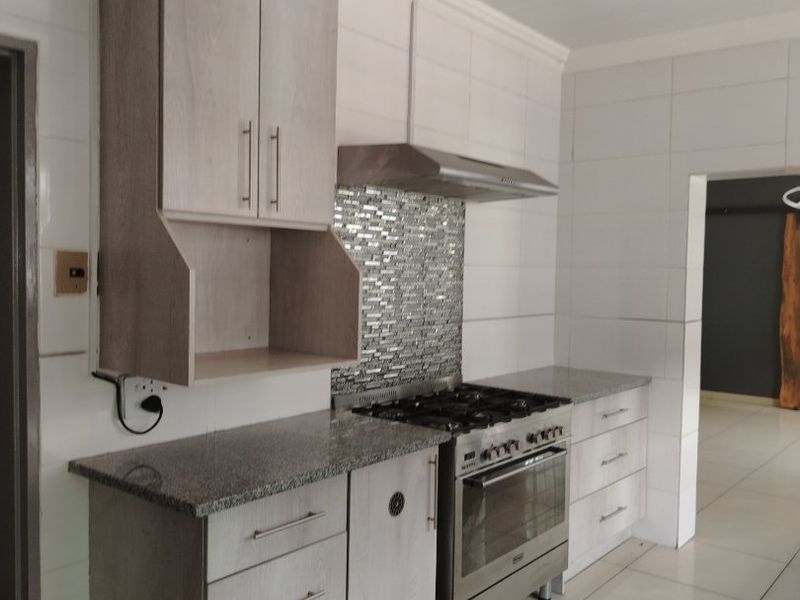 A clean, functional kitchen featuring light wood-finish cabinetry, granite countertops, a gas stove with extractor fan, and neutral tiled walls and floors.