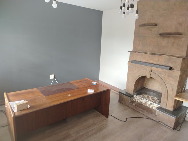 A living room featuring a prominent stone fireplace, laminate flooring, and neutral wall tones, offering a functional space with potential for modern updates.