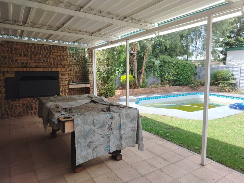 Covered patio area featuring a built-in braai, overlooking a garden and swimming pool with potential for maintenance and cosmetic upgrades.