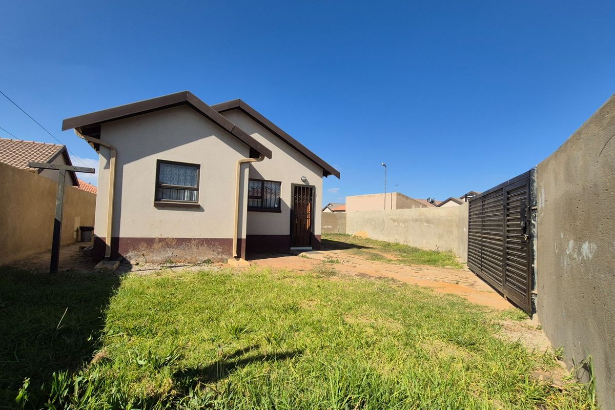 Rear view of the property featuring a small garden, perimeter wall, and metal sliding gate access.