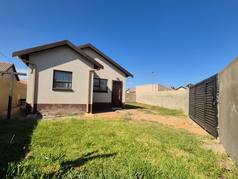 Rear view of the property featuring a small garden, perimeter wall, and metal sliding gate access.