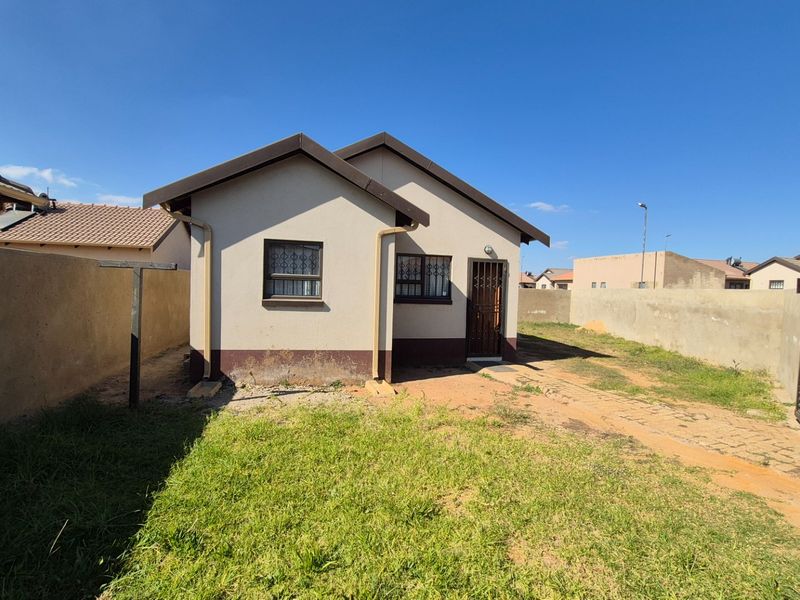 Rear view of a detached house featuring a small yard, perimeter walling, and security bars on windows and doors.
