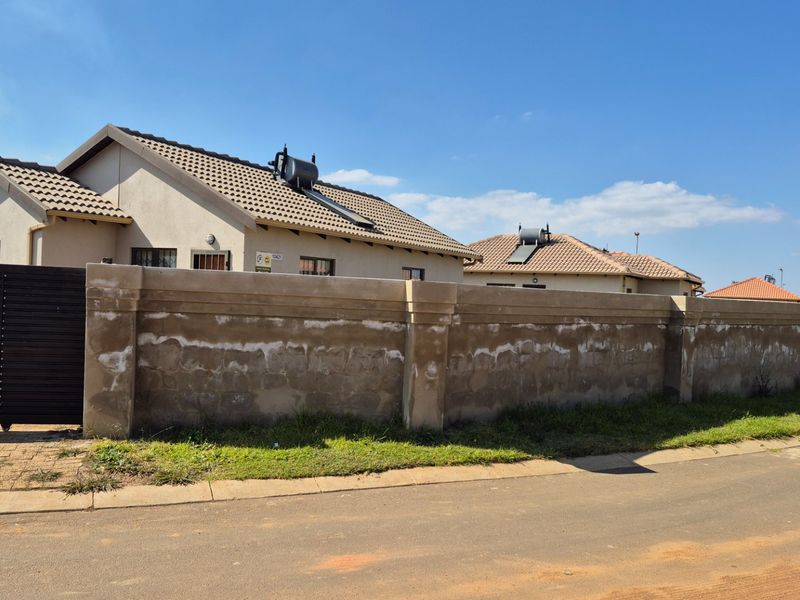 Front view of a residential property featuring a tiled roof, solar water heating system, and a prominent boundary wall.