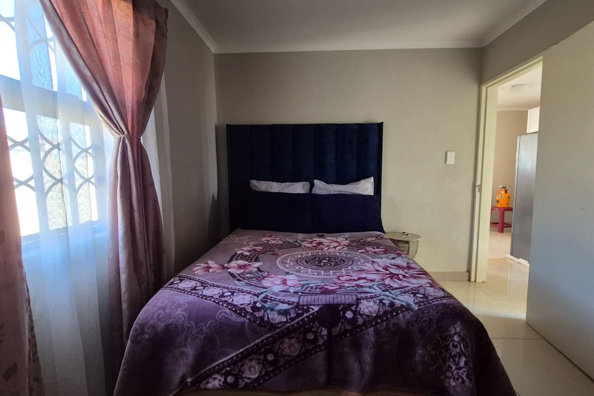 A functional bedroom featuring tiled flooring and a window with security bars, providing a simple and practical living space.