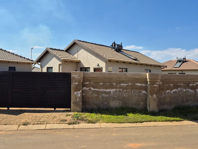 Front exterior view of a single-story house featuring a tiled roof, solar water heater, and a private perimeter wall with a sliding gate.