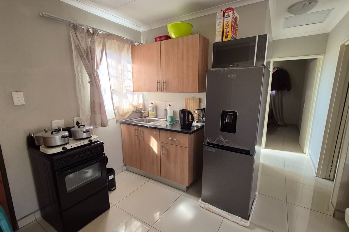 A compact kitchen featuring light wood-finish cabinetry, a stainless steel sink, tiled flooring, and a freestanding stove, providing a functional workspace.